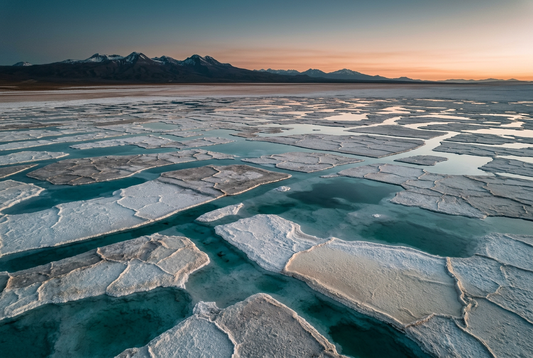AI-generated conceptual salt-flat landscape with turquoise water and distant mountains at sunrise, illustrating lithium sourcing.